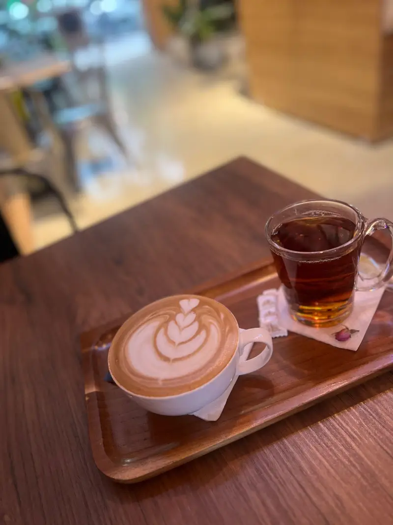 قهوه لاته آرت با طرح قلب و چای خوش‌رنگ سرو شده روی سینی چوبی در کافه پارس. تجربه‌ای دلنشین در محیطی آرام و ایده‌آل برای قرارهای دوستانه.