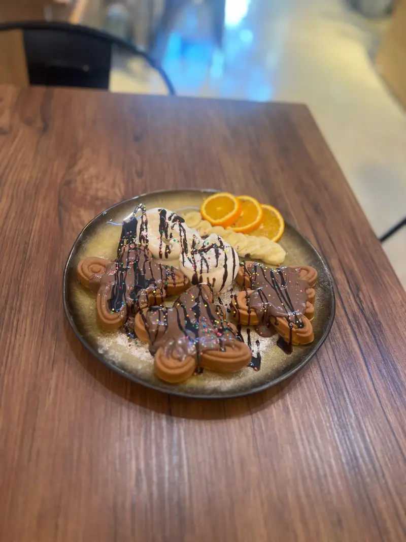 تصویری از وافل‌های دلپذیر کافه پارس: پوشیده از سس شکلات و بستنی، همراه با موز و پرتقال تازه. دسری محبوب برای دوستداران شیرینی.