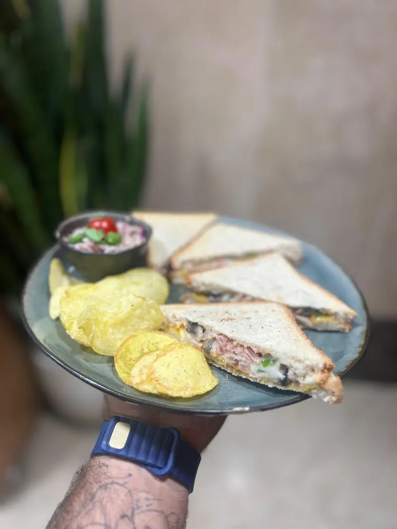 یک بشقاب بزرگ حاوی ساندویچ‌های کلاب تازه و لذیذ همراه با چیپس ترد و سس مخصوص در کافه پارس. انتخابی عالی از منوی غذای کافه.