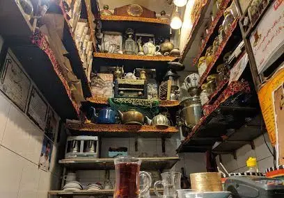 تصویری از داخل قهوه خانه تاریخی حاج علی درویش در بازار تهران، با قفسه‌های پر از اشیاء قدیمی، سماورهای برنجی و چای تازه دم.