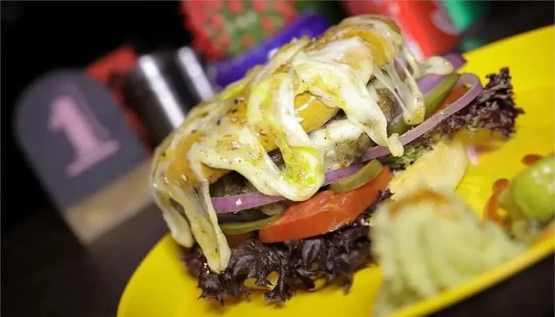 برگر لذیذ برگرجان با پنیر فراوان، کاهو، گوجه و پیاز قرمز روی بشقاب زرد، آماده سرو و تجربه‌ای خوشمزه از فست فود.