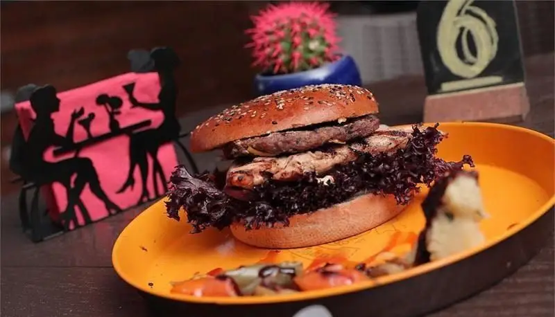 برگر بزرگ و خوشمزه برگرجان با دو نوع پتی، کاهو قرمز تازه و نان کنجدی روی بشقاب نارنجی، آماده سرو در محیط رستوران.