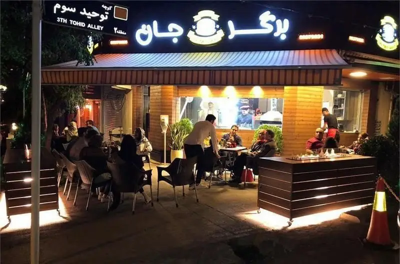 تصویری شبانه از رستوران برگرجان در کوچه توحید سوم، با تابلوی نئونی درخشان و مشتریان حاضر در فضای باز، مکانی عالی برای تجربه برگرهای لذیذ.