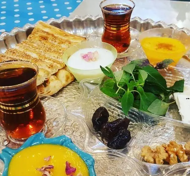 یک سفره صبحانه سنتی و ایرانی از سفره خانه وسنت سرای حافظ، شامل نان کنجدی، چای، پنیر، سبزی، گردو، آلو خشک و دسرهای خوشرنگ.