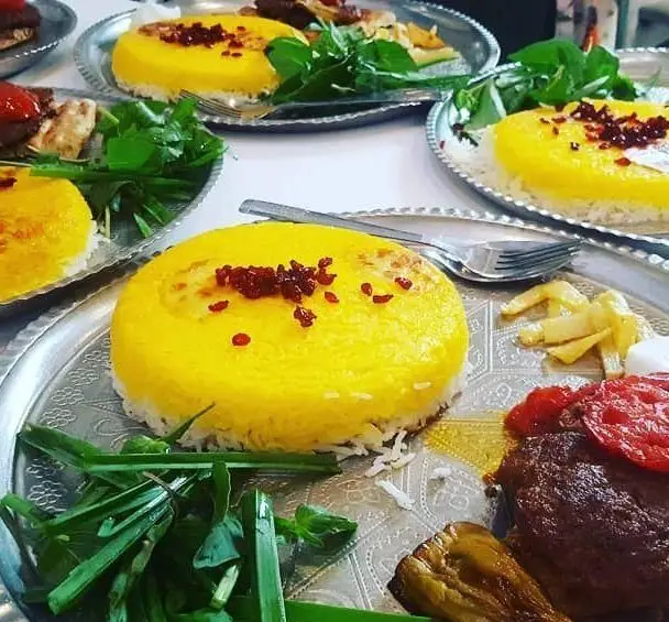 سفره خانه وسنت سرای حافظ: میز شام با زرشک پلو زعفرانی، کباب، گوجه و بادمجان کبابی، سبزیجات تازه. لذت غذای اصیل ایرانی در رستوران سنتی حافظ.