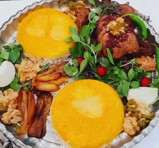 سفره خانه و سنت سرای حافظ: بشقاب غذای سنتی ایرانی با برنج زعفرانی، ته دیگ، خورشت گوشت، بادمجان، سبزی تازه و ترشی.