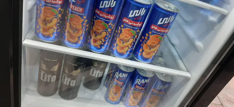 یخچال خنک پر از نوشیدنی‌های انرژی‌زا لایف و آبمیوه رانی هلو در گیم‌نت VIP PS5 پارس برای مشتریان.