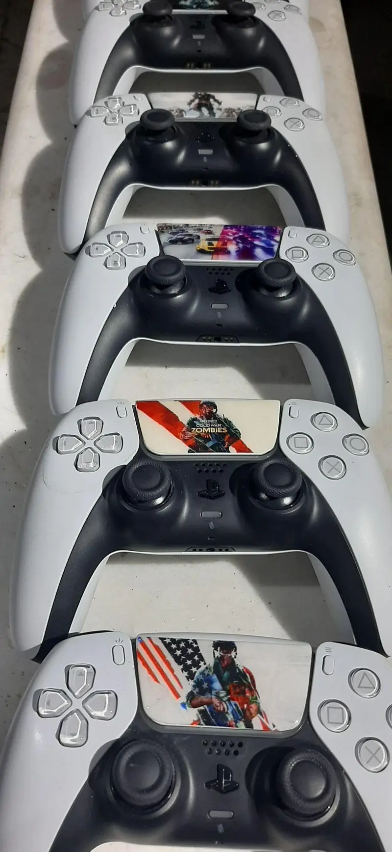 صفی از کنترلرهای PS5 DualSense سفید و مشکی با تاچ‌پدهای طرح‌دار برای گیم‌نت VIP PS5 پارس. بهترین تجربه بازی پلی‌استیشن 5 را ارائه می‌دهد.