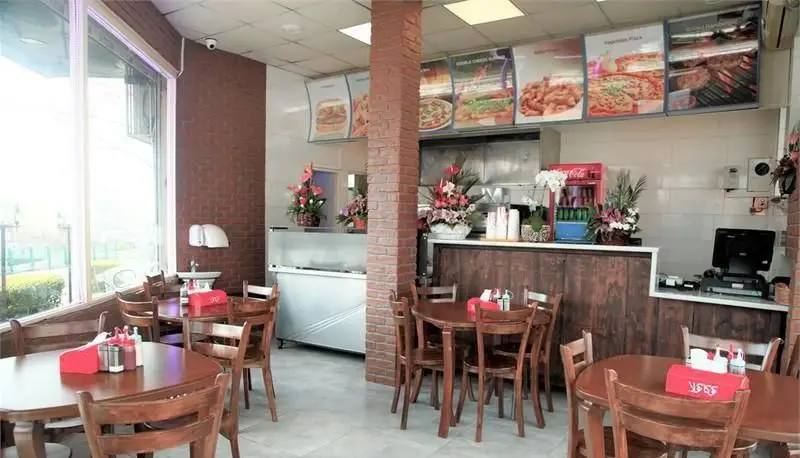 فضای داخلی پیتزایی پیتزا بلا با میز و صندلی‌های چوبی، منوی متنوع پیتزا، برگر و فست فود، محیطی دنج و دوستانه برای تجربه غذایی دلپذیر.