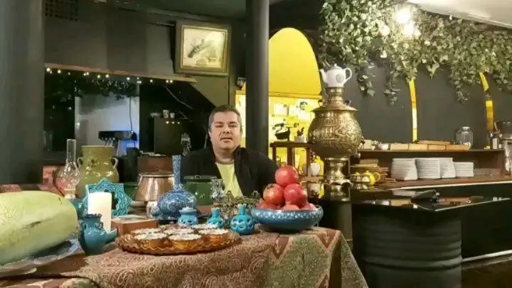 صاحب هوم برگر در محیط رستوران سنتی با میز یلدا، هندوانه، انار، سماور و دکوراسیون زیبا. فضایی دلنشین برای مشتریان.