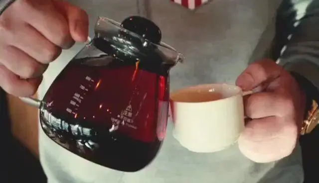 سرو نوشیدنی تازه و باکیفیت در هوم برگر: تصویری دلنشین از ریختن قهوه یا چای گرم از کتری شیشه‌ای به فنجان، تجربه‌ای دلپذیر برای مشتریان.