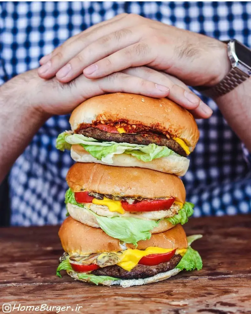 عکس سه همبرگر سه طبقه هوم برگر با پنیر، کاهو، گوجه و قارچ، آماده سرو. بهترین همبرگرهای خوشمزه را از ما بخواهید.