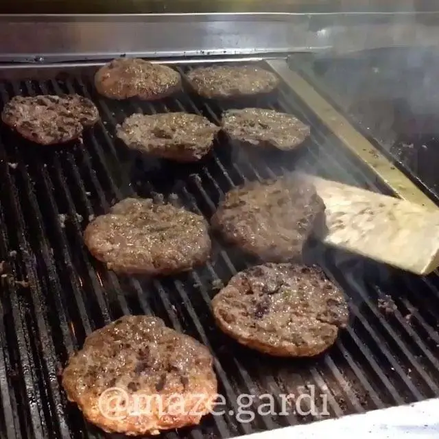 طبخ پتی های برگر گوشت دست ساز و تازه هوم برگر روی گریل حرفه‌ای و داغ، آماده سازی سریع برای سرو در بهترین فست فود.