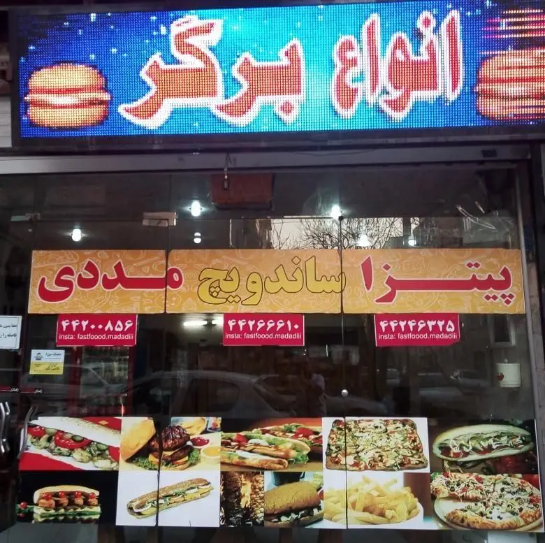 نمای بیرونی فست فود پیتزا مددی با تابلو انواع برگر، پیتزا و ساندویچ مددی، همراه با تصاویر جذاب غذاها و اطلاعات تماس.