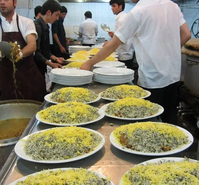 کارکنان مشغول آماده‌سازی انبوهی از پلوهای سنتی ایرانی با برنج زعفرانی در آشپزخانه رستوران پیتزا مددی برای سرویس سریع