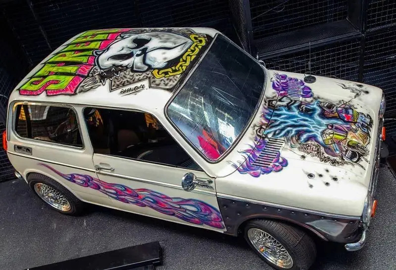 ماشین سفید سفارشی کافه خیابون با گرافیتی هنری: طرح اسکلت، رعد و برق و شعله‌های رنگارنگ روی بدنه خودروی کلاسیک.
