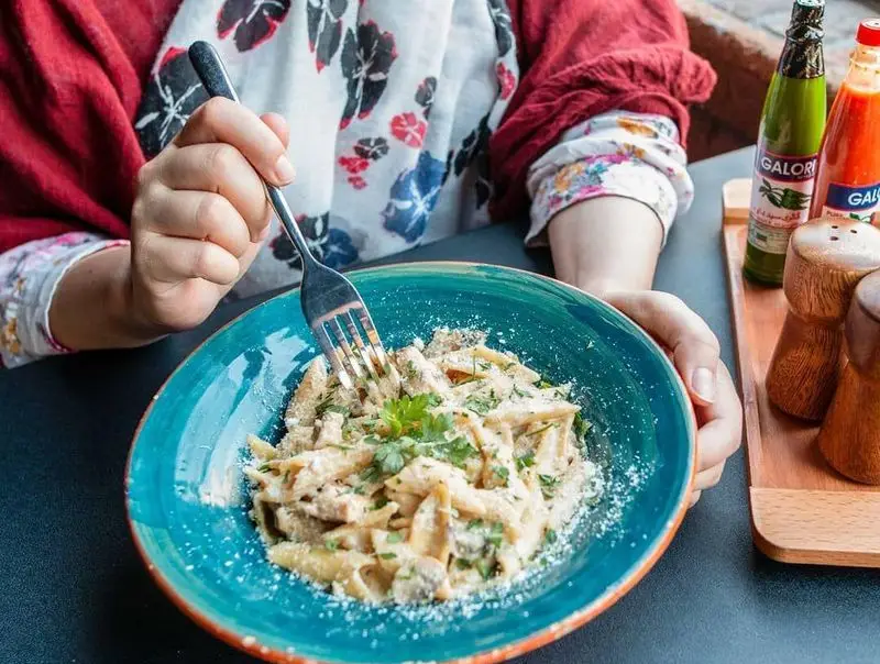 مشتری در کافه خیابون مشغول خوردن پاستای خوشمزه با سس سفید و پنیر پارمزان است. محیط دلنشین کافه و غذای باکیفیت.