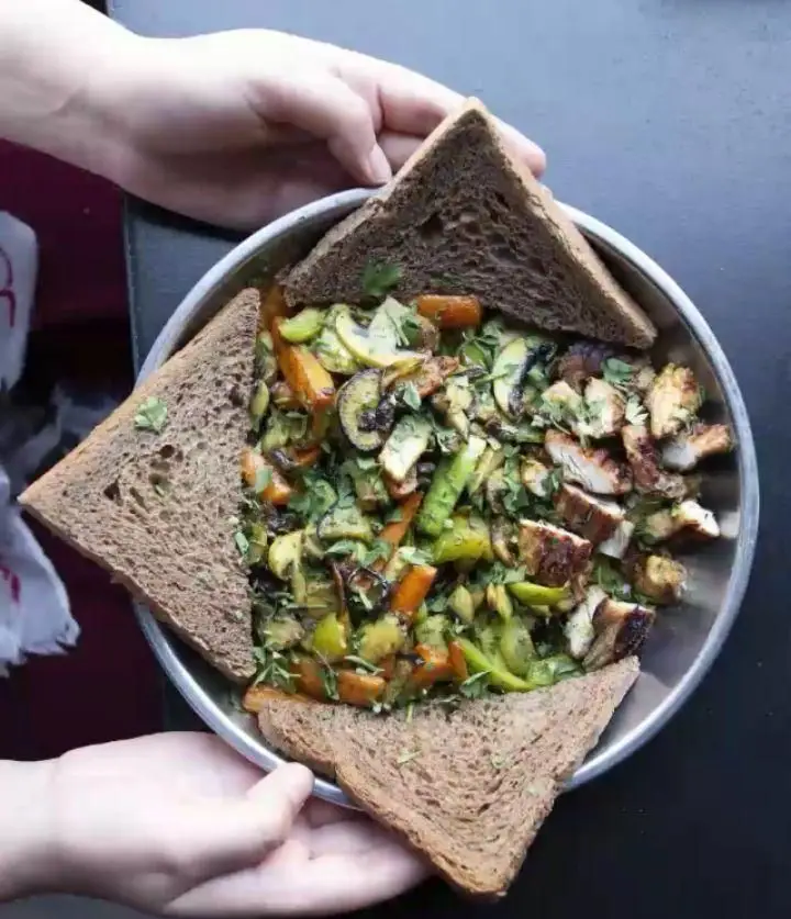 غذای خاص کافه خیابون: مرغ گریل، سبزیجات تفت داده شده (قارچ، هویج، فلفل) با چیدمان هنرمندانه نان قهوه ای دور بشقاب. سالم و خوش طعم.