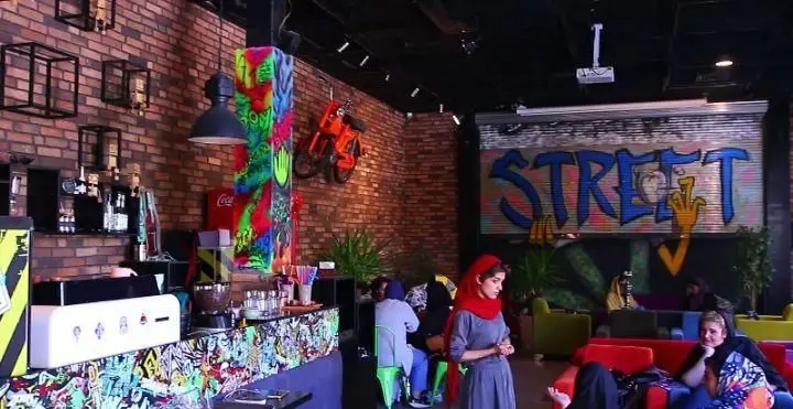 کافه خیابون: دکوراسیون داخلی جذاب با دیوارهای آجری، گرافیتی رنگارنگ، موتور سیکلت تزئینی و فضای صمیمی برای دورهمی جوانان.