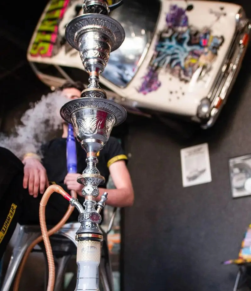 مشتری در کافه خیابون مشغول کشیدن قلیان با دود غلیظ، در فضایی با دکوراسیون هنری و منحصر به فرد. ماشین روی دیوار دیده می‌شود.