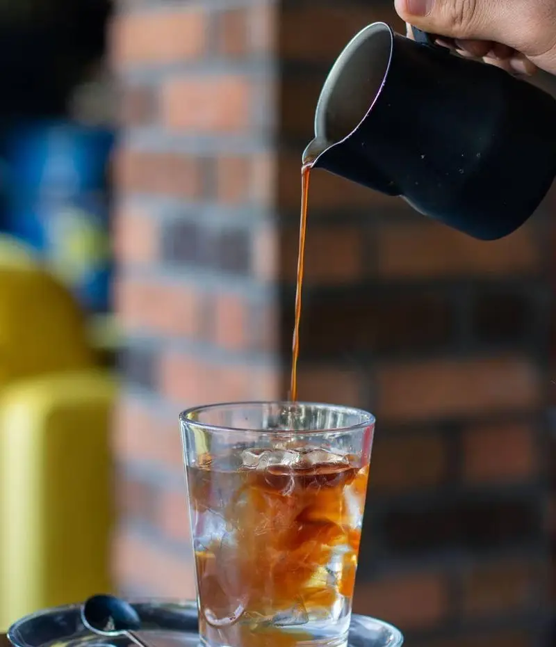 تهیه کولد برو یا آیس کافی خنک و دلچسب در کافه خیابون. دست در حال ریختن قهوه غلیظ به لیوان پر از یخ و آب.