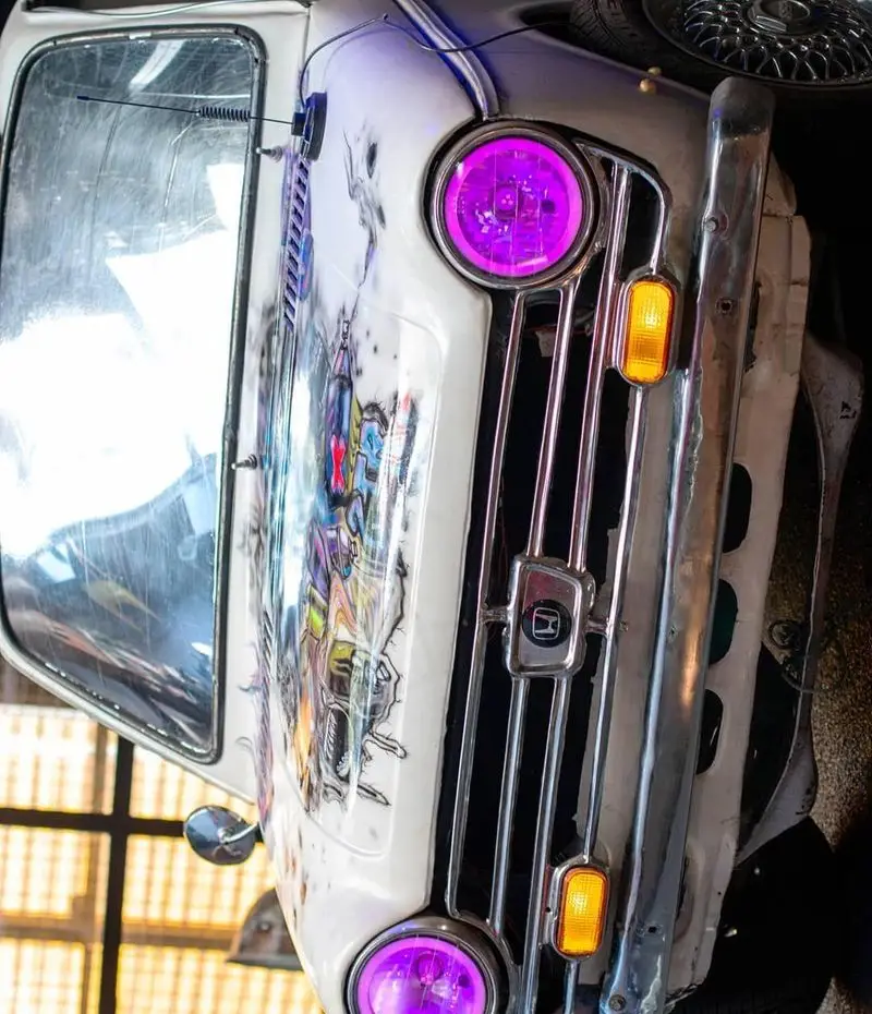 نمایی نزدیک از دکوراسیون خاص کافه خیابون، با ماشینی کلاسیک مزین به گرافیتی رنگارنگ، چراغ‌های بنفش و جلوپنجره کروم، فضایی هنری و دلنشین.