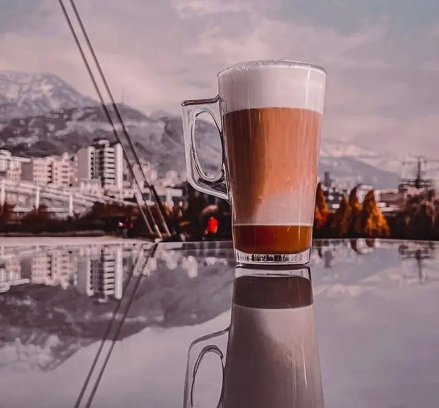 نوشیدنی لاته دلنشین کافه فلورین با منظره کوهستانی شهر. تجربه قهوه‌ای خاص در فضای زیبای کافه Florin.