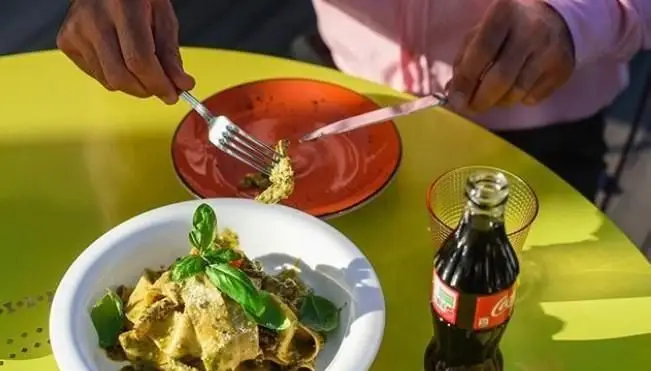 میهمانی در کافه فلورین از پاستای باکیفیت با سس سبز و تزئین ریحان تازه لذت می‌برد. کوکاکولا و فضای شاداب میز زرد، تجربه‌ای کامل.