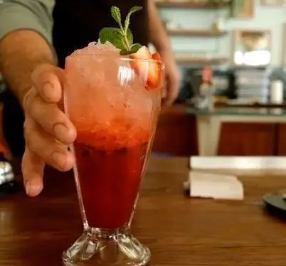 سرو نوشیدنی خنک و دلچسب توت فرنگی با یخ و برگ نعنای تازه توسط پرسنل کافه فلورین روی میز چوبی. لذت نوشیدنی تابستانی.