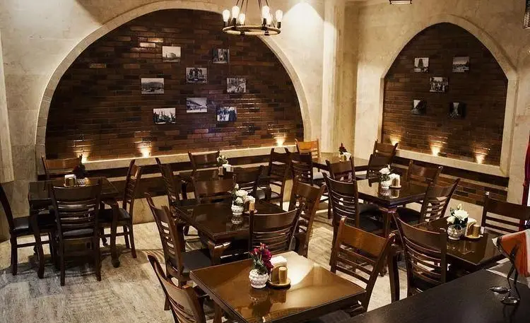 فضای داخلی شیک و دنج رستوران مارینو با دکوراسیون سنتی، شامل دیوارهای آجری قوسی، میز و صندلی‌های چوبی تیره و نورپردازی گرم و دلنشین.