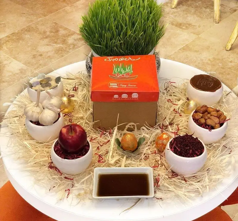 هفت سین نوروزی خلاقانه با سبزه، سیب، سیر، سمنو، سماق، سکه و هدایای جذاب از برند برگر اسلاید برگر.