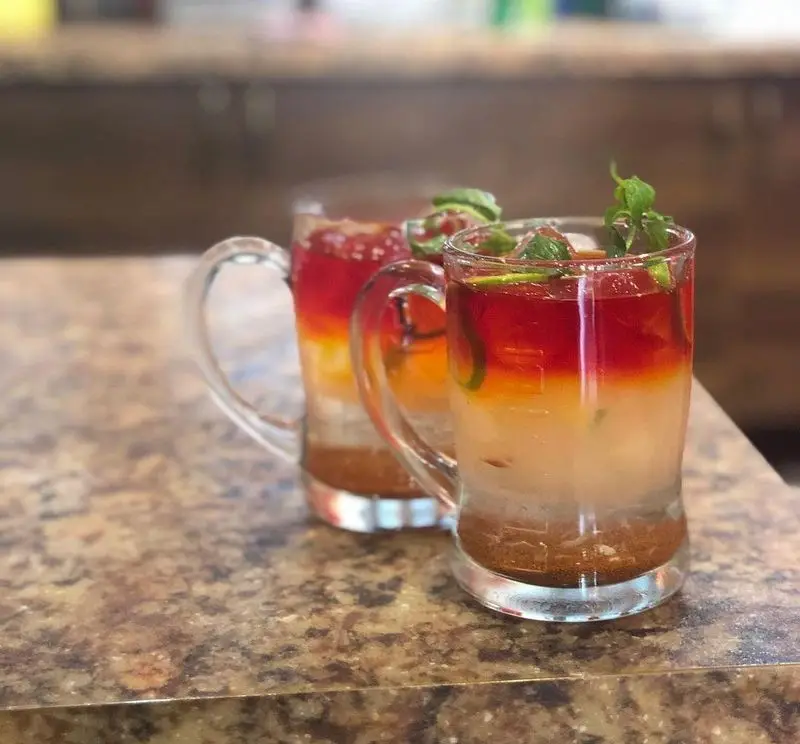 دو نوشیدنی خنک و لایه‌لایه با رنگ‌های جذاب در لیوان‌های شیشه‌ای روی میز رستوران ایتالیایی ژولی، تجربه‌ای تازه و خاص.