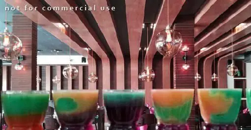 نوشیدنی‌های لایه‌ای متنوع در فضای داخلی لوکس کافه رستوران بلوبیسترو با دکوراسیون مدرن، سقف چوبی خاص و نورپردازی زیبا.