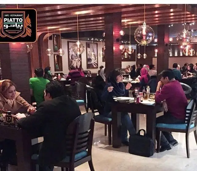 تصویری از فضای داخلی شلوغ کافه رستوران بلوبیسترو، مشتریان در حال صرف غذا و نوشیدنی در محیطی دلنشین با دکوراسیون چوبی و چراغ‌های آویز.