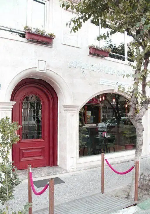 نمای ورودی رستوران ایتالیایی لان چای با درب چوبی قرمز رنگ قوسی، پنجره بزرگ کافه، گلدان‌ها و درختچه، محیطی گرم و دعوت‌کننده.