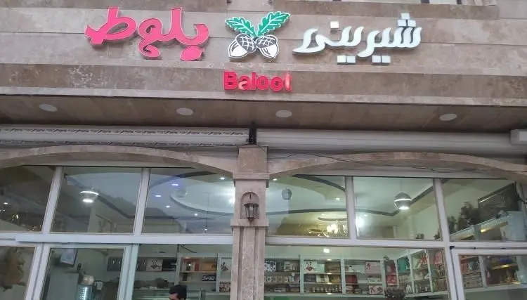 نمای شیک و مدرن بیرونی شیرینی فروشی بلوط، با تابلوهای فارسی و انگلیسی "Balool" و لوگوی جذاب بلوط در بالای ورودی اصلی.