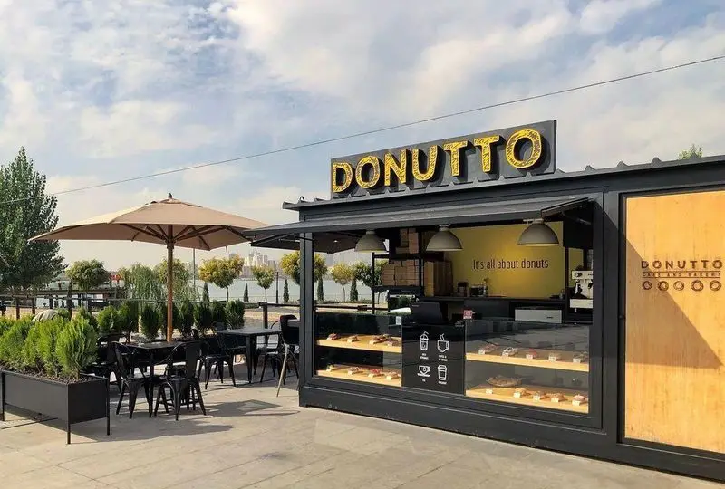 کافه دوناتو بام لند، یک کافه مدرن با فضای باز شامل میز و صندلی، واقع در کنار دریاچه چیتگر، مناسب قهوه و دونات.