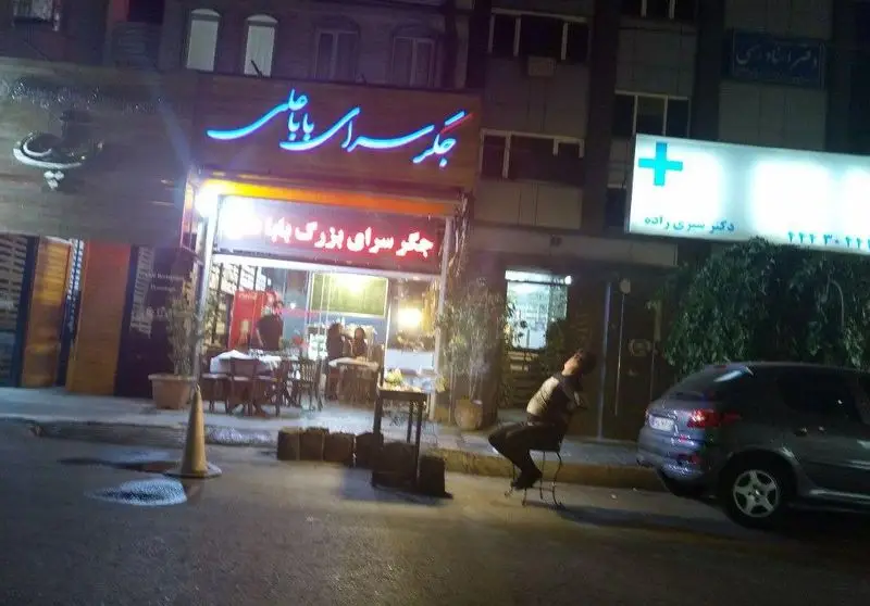 تصویری شبانه از جگرسرای بزرگ باباها، معروف به جگرسرای بابا علی، با تابلوی نئونی چشمگیر و فضای داخلی دلپذیر آماده سرو جگر تازه.