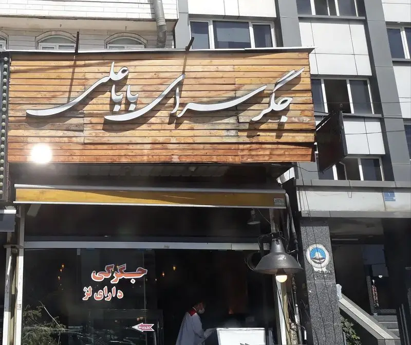نمای بیرونی جگرسرای بابا علی، رستوران جگرکی با تابلوی چوبی جذاب و ورودی دارای لژ برای غذای ایرانی.