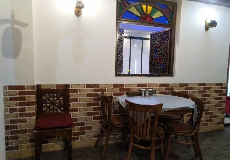 فضای داخلی جگرسرای بابا علی با دکوراسیون سنتی، شامل میز و صندلی چوبی، دیوار آجری و پنجره ارسی رنگی، محیطی دلنشین برای میزبانی.