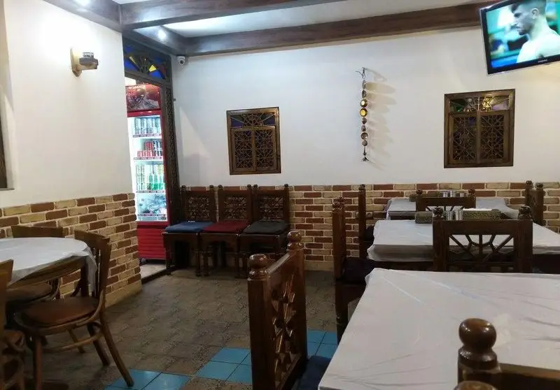 فضای داخلی دنج و سنتی جگرسرای بابا علی با میز و صندلی‌های چوبی، دیوارهای آجری و یخچال نوشیدنی. مکانی دلنشین برای صرف جگر.