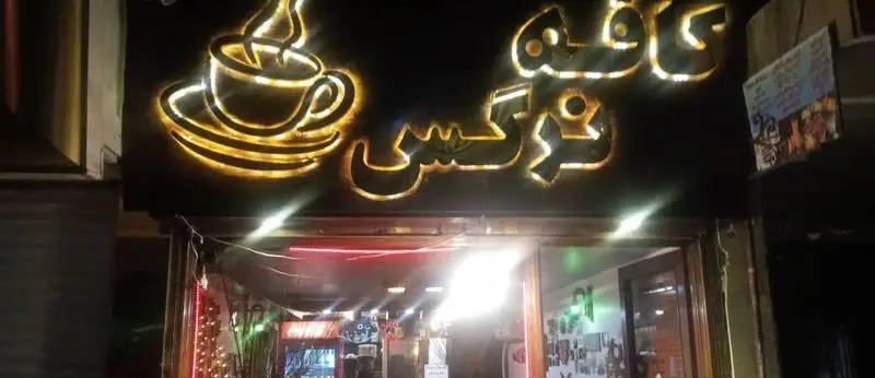 ورودی کافه اثر در شب با تابلوی نئونی برجسته کافه و فنجان قهوه، دعوت کننده به فضایی گرم و دوستانه برای تجربه قهوه اصیل.