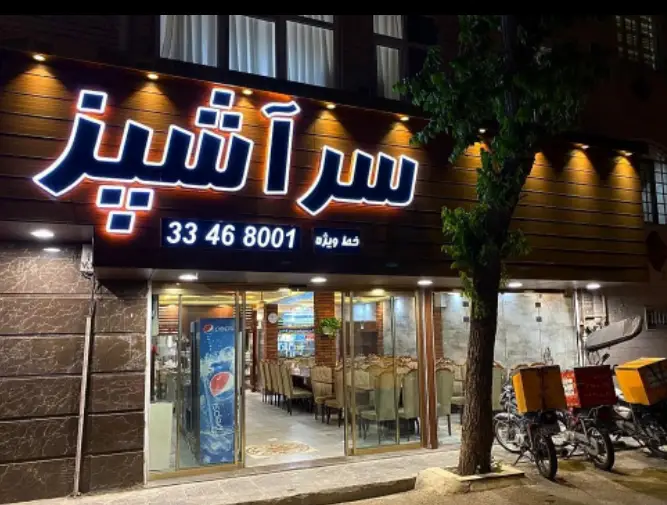 تصویری از نمای شبانه رستوران سر آشپز با تابلوی روشن، ارائه دهنده غذای ایرانی باکیفیت و سرویس دلیوری سریع، به همراه شماره تماس ویژه ۳۳۴۶۸۰۰۱.