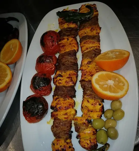 بشقاب کباب میکس رستوران سرآشپز شامل جوجه کباب و کباب گوشت با گوجه کبابی، زیتون و پرتقال. غذای ایرانی لذیذ.
