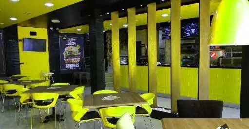 نمای داخلی فست فود آماندا با دکوراسیون مدرن زرد و مشکی، میز و صندلی‌های روشن، پیشخوان سفارش و پوستر برگر بزرگ.