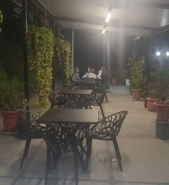 کافه اسکواش برج میلاد در شب: فضایی دلنشین و سرسبز با میز و صندلی‌های شیک، گیاهان آویز و گلدان‌های تزئینی در محیط باز.