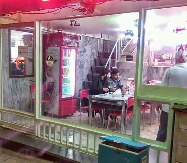 سرای افق: نمای رستوران با شیشه‌های بزرگ، مشتریان مشغول صرف غذا و نوشیدنی، یخچال پر از نوشیدنی، فضایی دنج و مدرن.