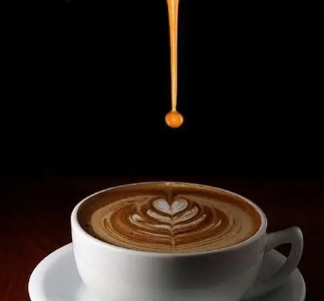 فنجانی از لاته داغ با لاته آرت هنرمندانه از کافه باران. قطره‌ای طلایی در حال فرود آمدن روی سطح قهوه.