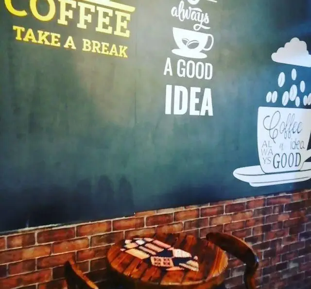 تصویر جذاب از دیوار و میز چوبی کافه باران با شعار "قهوه همیشه ایده خوبی است"، مکانی عالی برای یک استراحت دلپذیر.