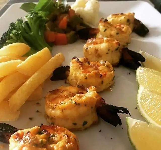 میگو گریل شده خوش‌طعم با سیب زمینی سرخ کرده، کلم بروکلی، سبزیجات و لیمو. تجربه بی‌نظیر غذای دریایی در ایوان رستوران.